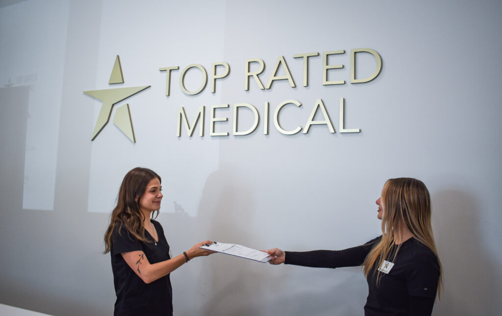 Two woman passing a clipboard to each other in the Top Rated Medical lobby